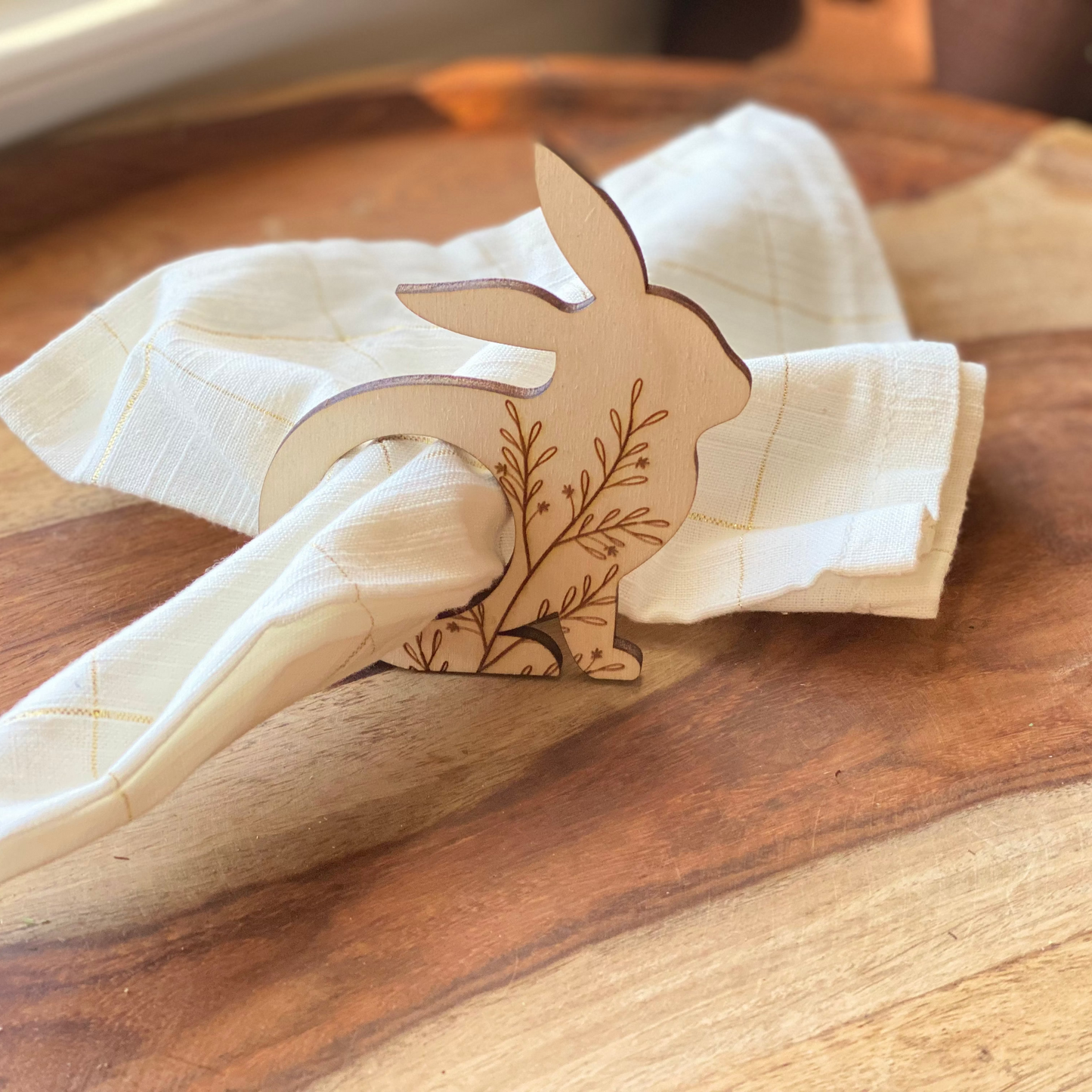 Wooden bunny-shaped napkin holder with a floral design on a white napkin, placed on a wooden surface.